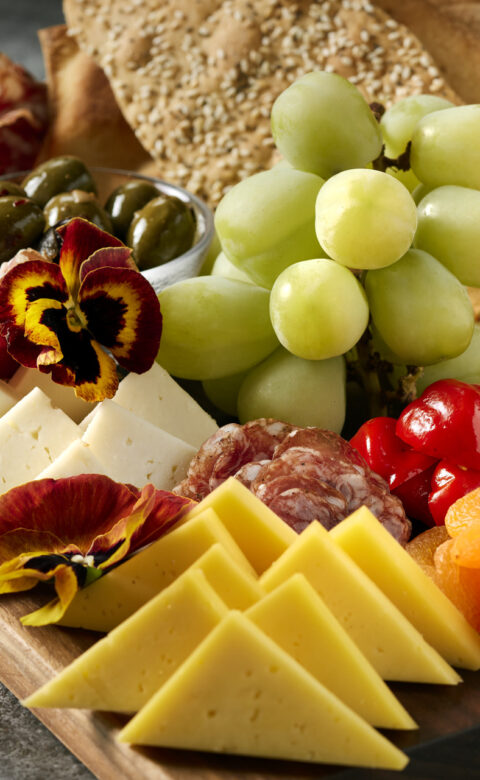 a platter of cheese, meats, fruit, and a cocktail