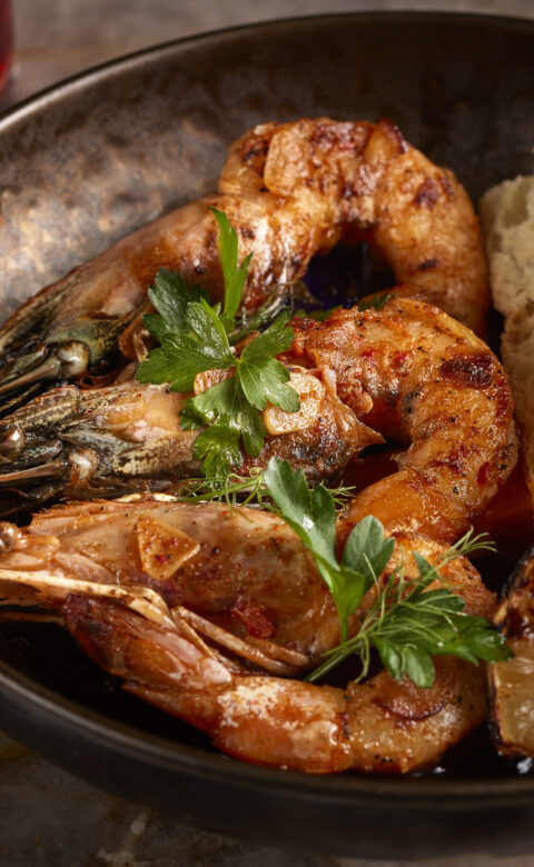 a bowl filled with shrimp and bread next to a glass of wine