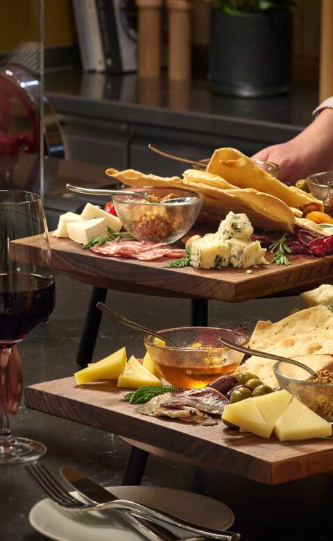 a large platter with fresh meats and cheeses being served to a woman holding a wine glass